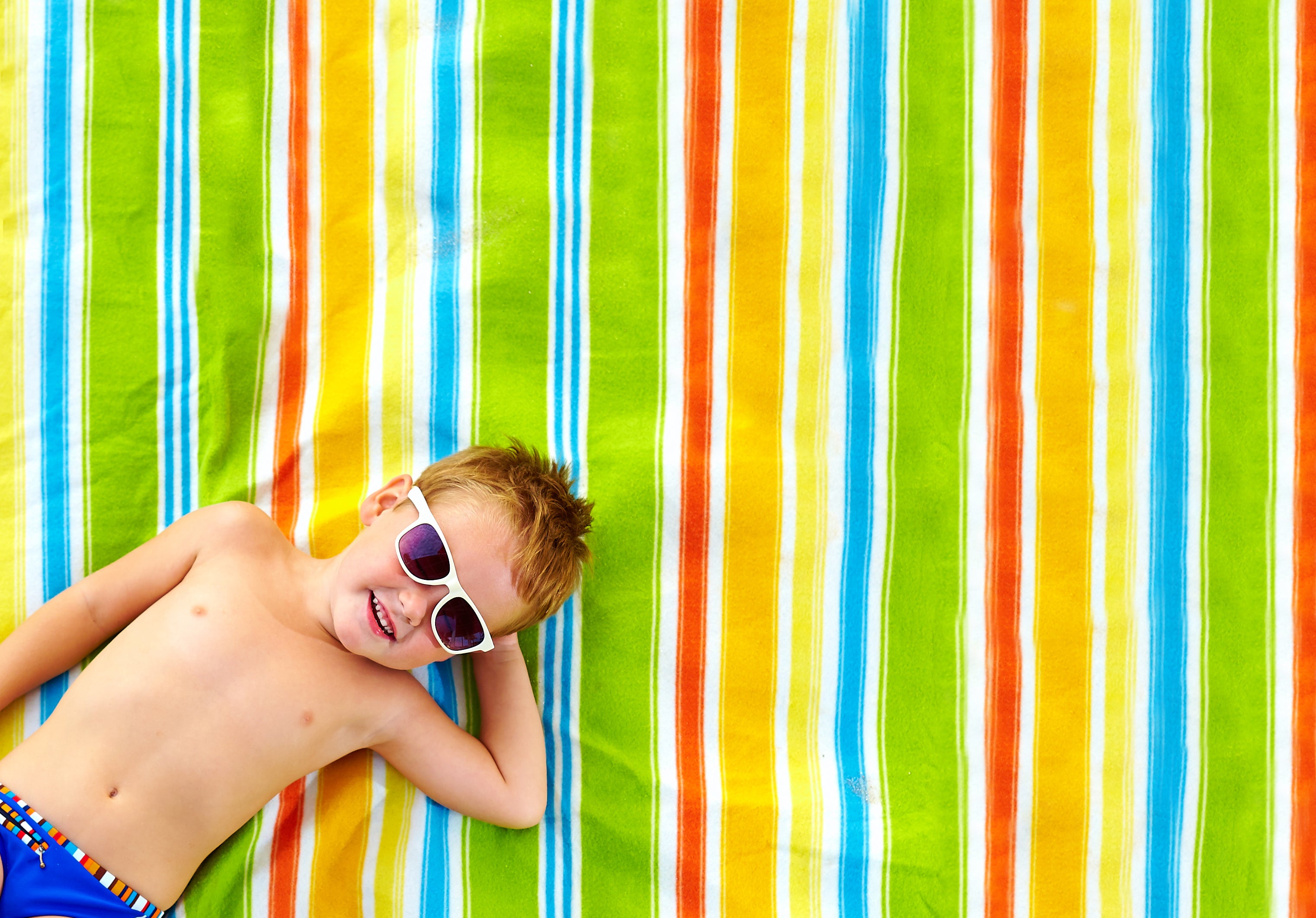 happy kid sunbathing on colorful blanket