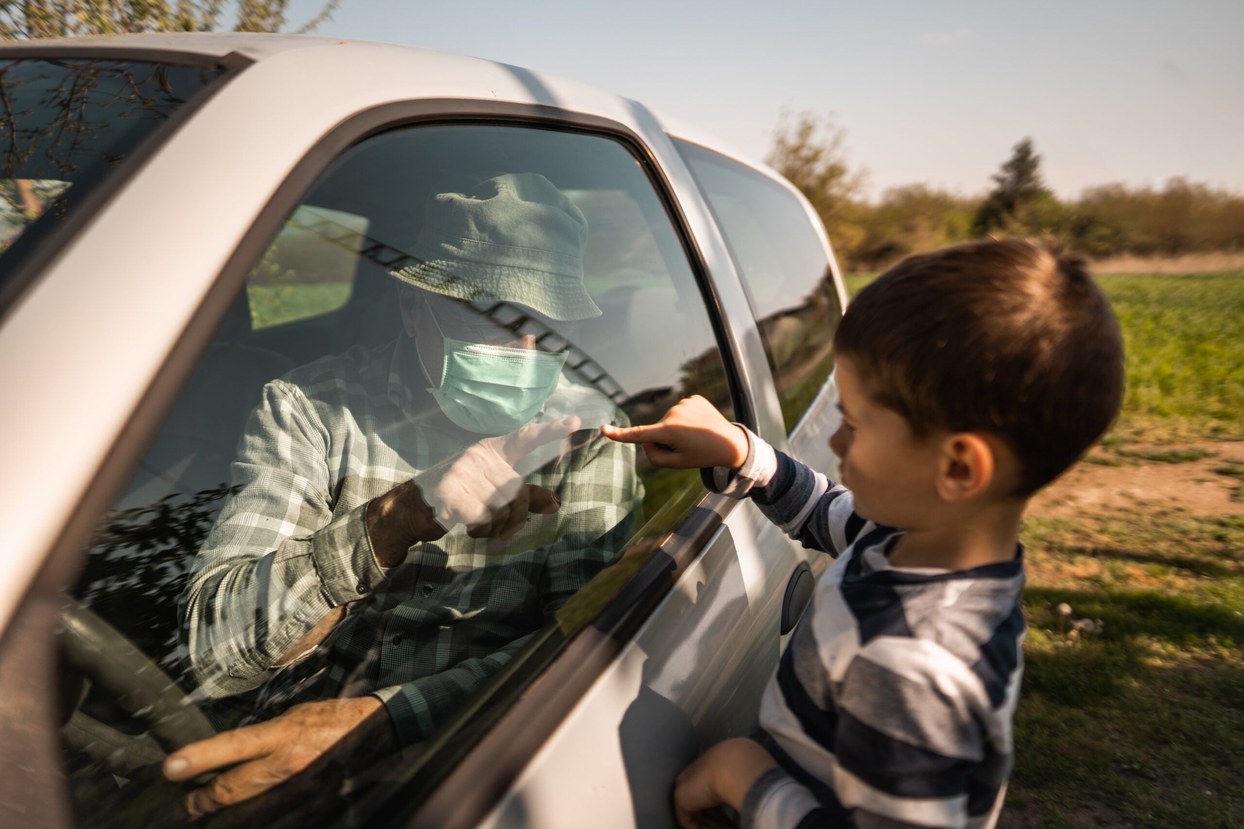 Grandfather and grandson, greeting through car window during coronavirus pandemic