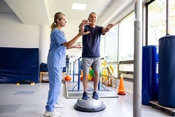 Man doing exercises using a balance ball with the help of his physical therapist