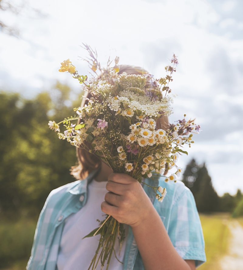 Person in a field with flowers in front of their face