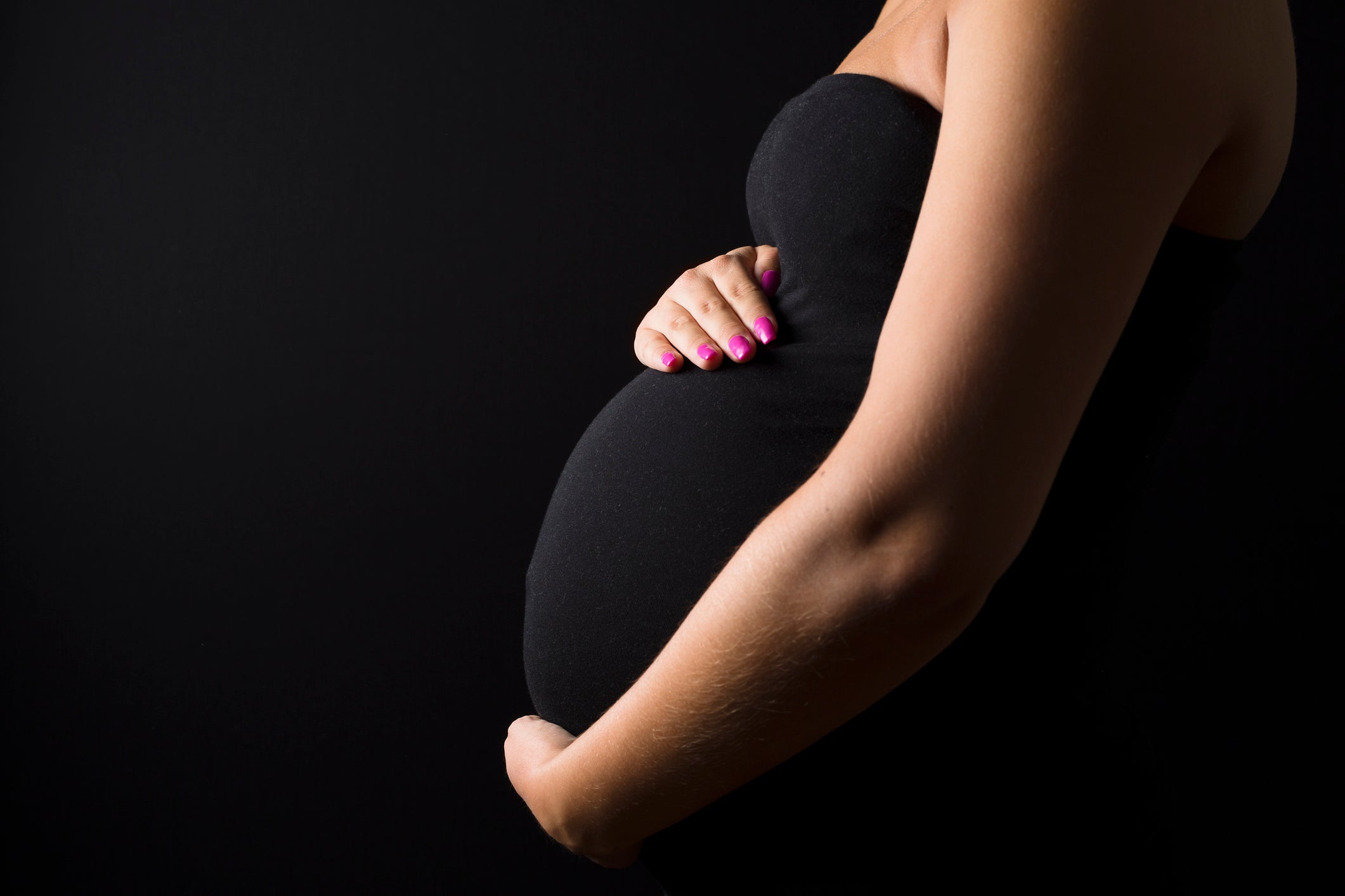 Young pregnant woman stands with her hands at the belly