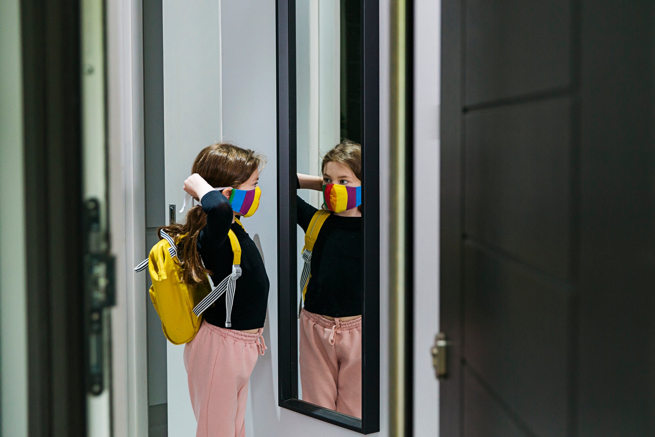 Young girl putting on her face mask in mirror by front door
