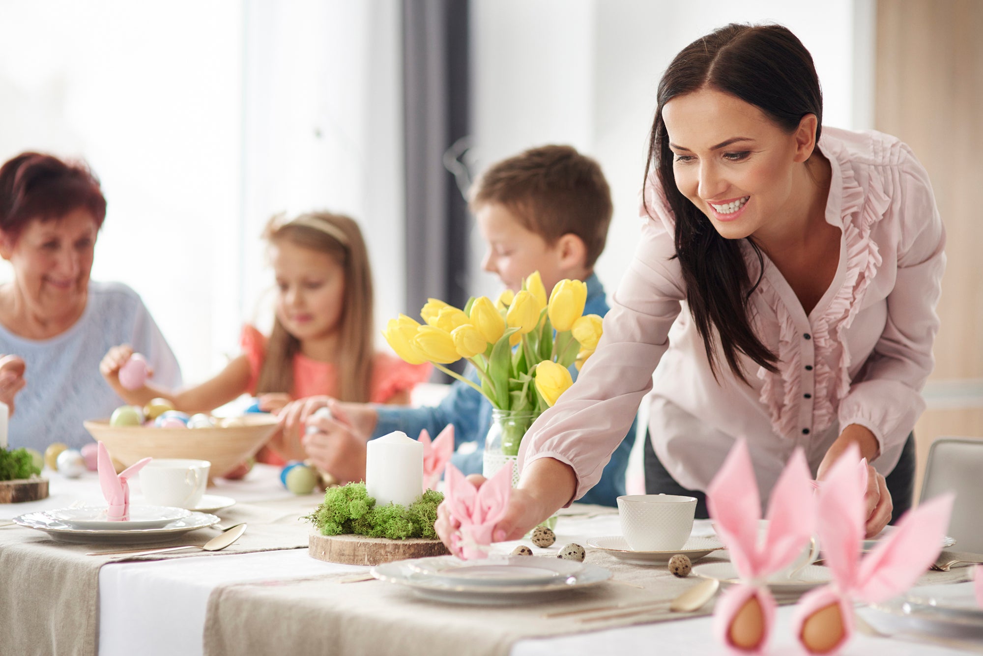 Woman and family preparing place settings at easter dining table