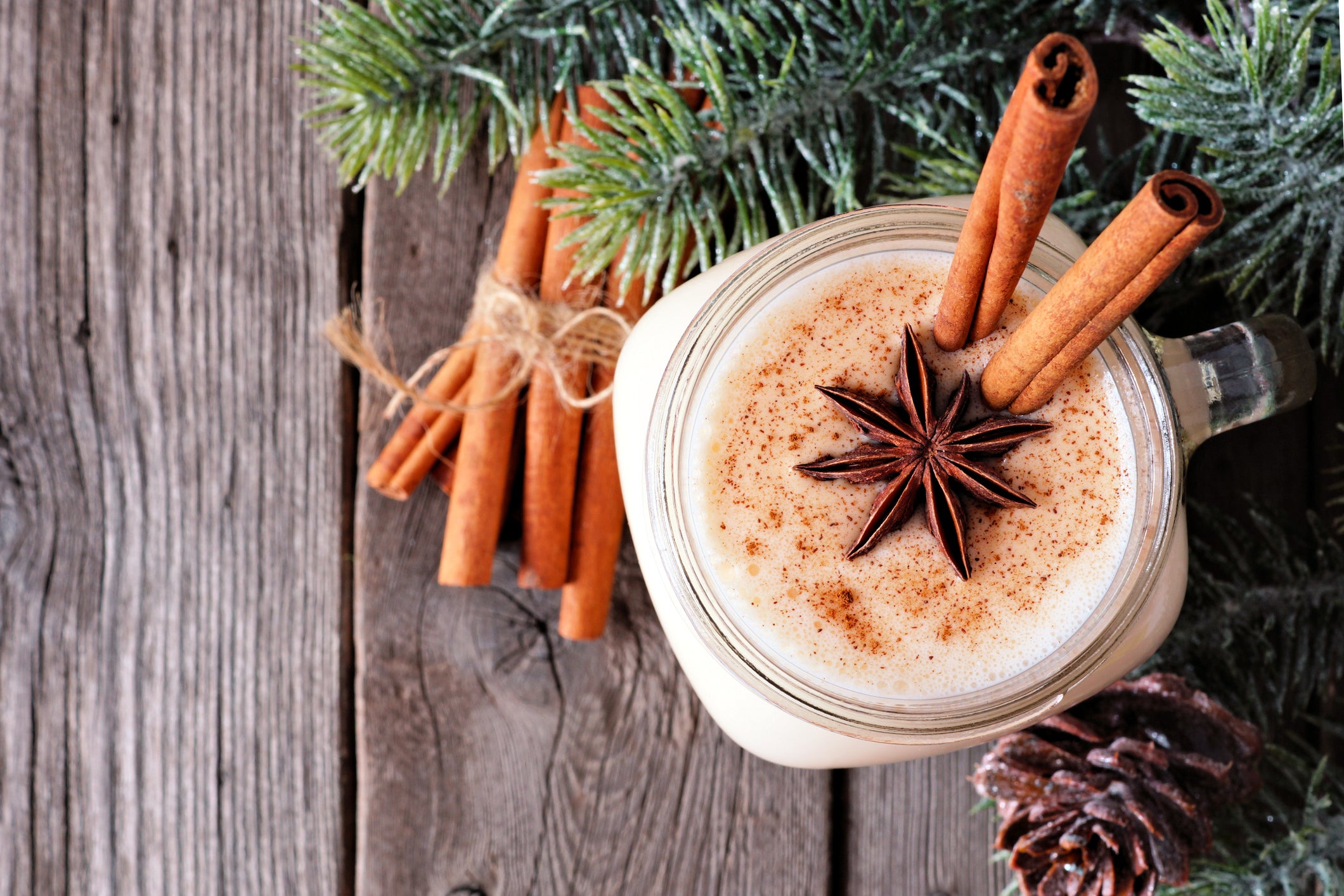 Christmas eggnog in a mason jar, above view with tree branches on wood