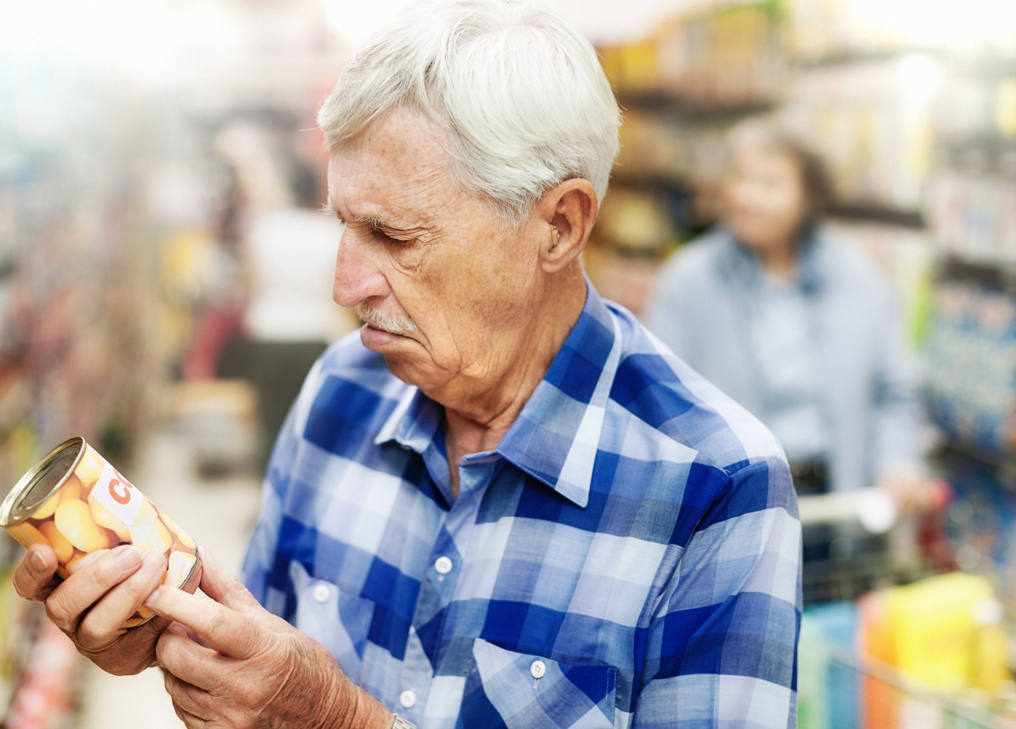 Senior man examines can of corn in supermarket