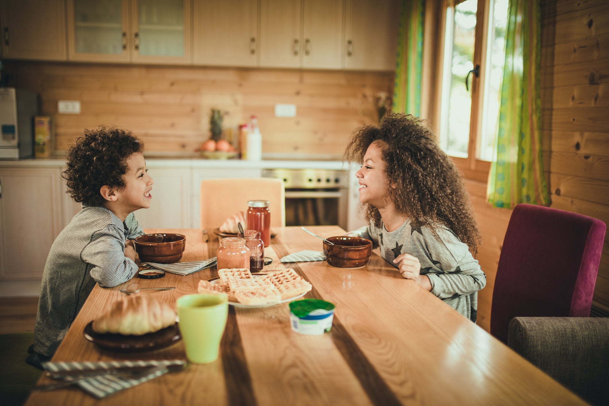 Cute African American kids talking while having breakfast at dining table.