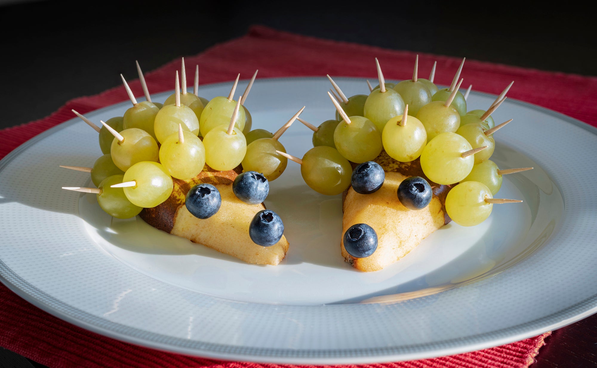 Grape, pear and blueberries fruit in shape of fun hedgehog in white plate
