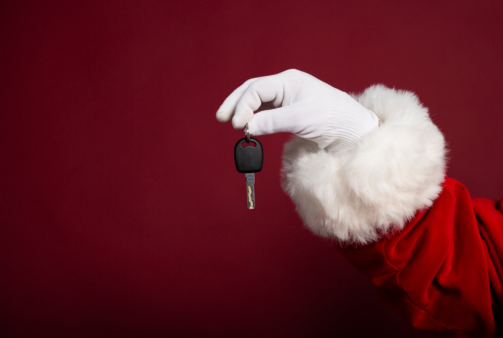 Male hand in white glove and Santa Clause costume holding key on red background, Christmas and New year concept