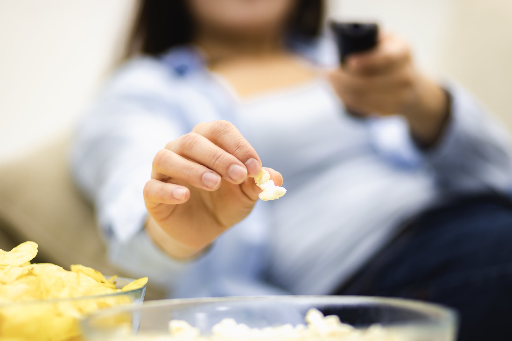 Unrecognizable woman is eating pop corn. Close up huge deep plates, full of pop corn and potato chips.
