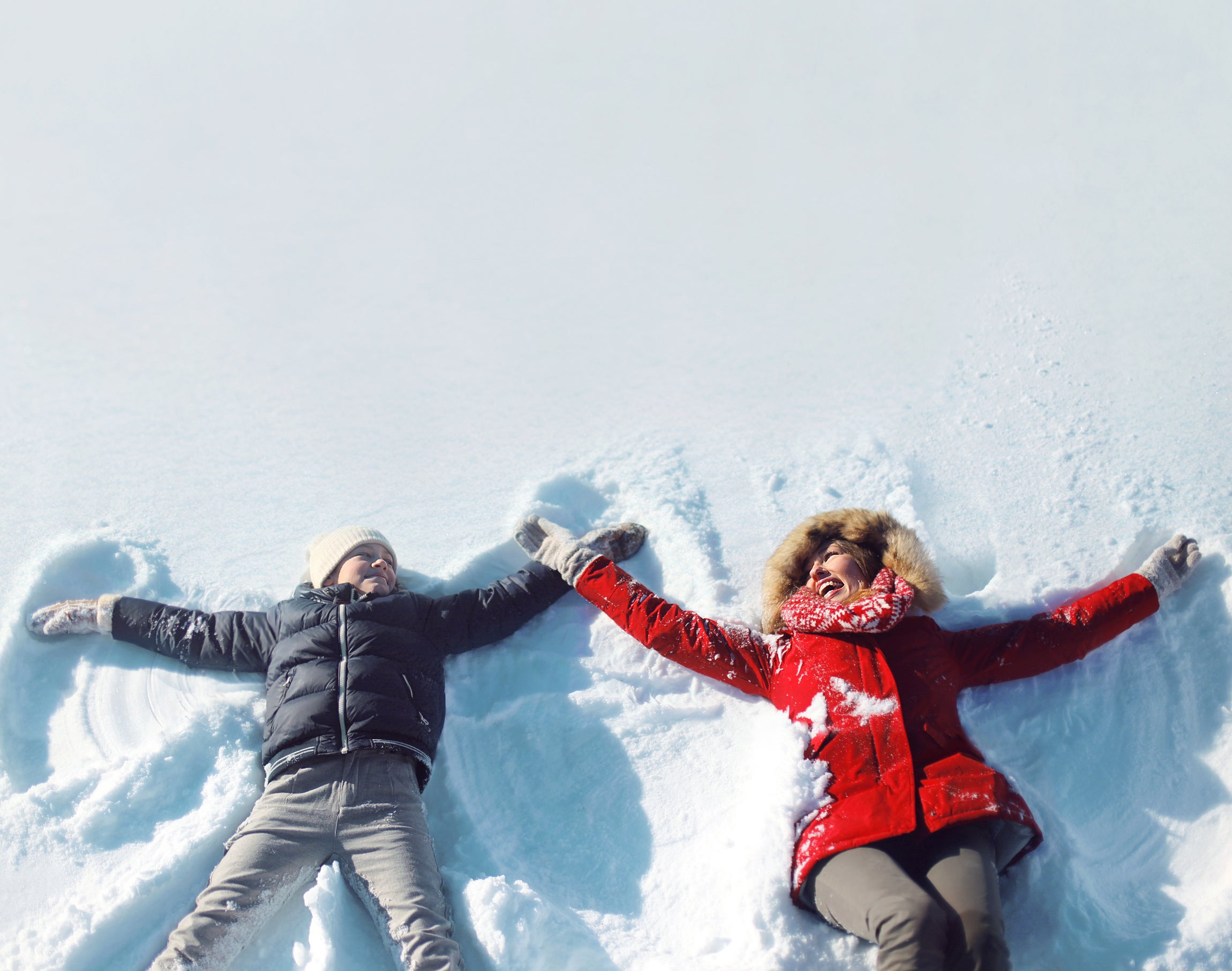 Happy mother, son playing having fun lying in snow winter
